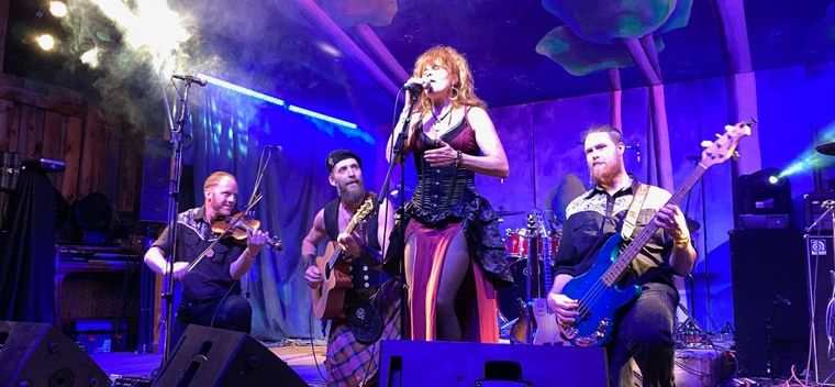 Dream Heavy on a festival stage: a singer at the microphone with a fiddler, a guitarist and a bassist beside her, under blue and purple light